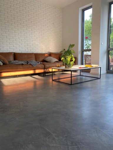 Moderne Wohnzimmer mit einem braunen Sofa, Tisch und Pflanzen bei Tageslicht.