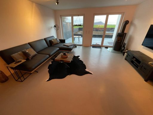 Moderne Wohnräume mit Zementboden, einer Couch, Couchtisch und großen Fenstern.