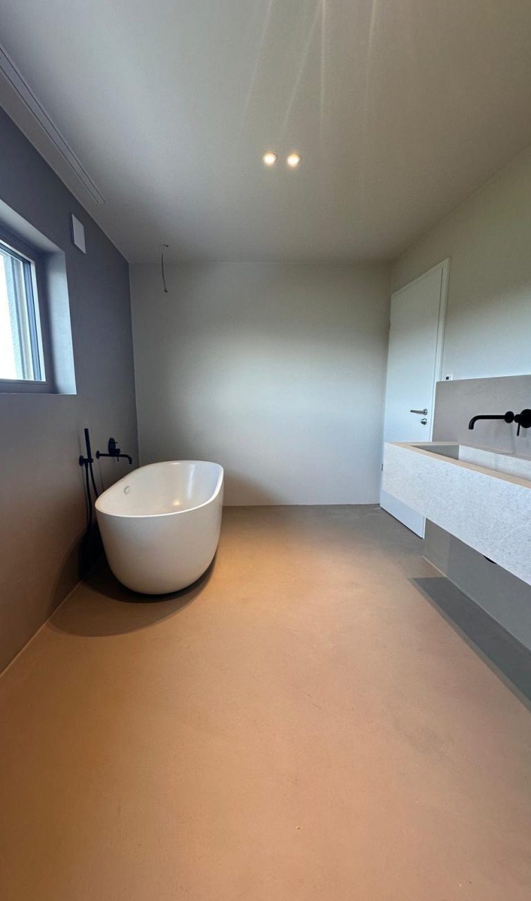 Modernes Badezimmer mit Mikrozement, freistehender Badewanne und einfacher Waschbeckenanlage.