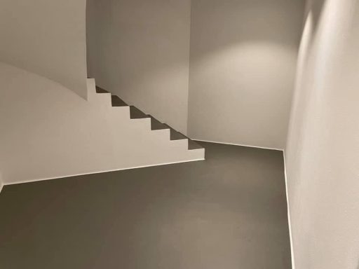 Abgeschrägter Raum mit Treppe und sanften, neutralen Farben an Wänden und Boden.